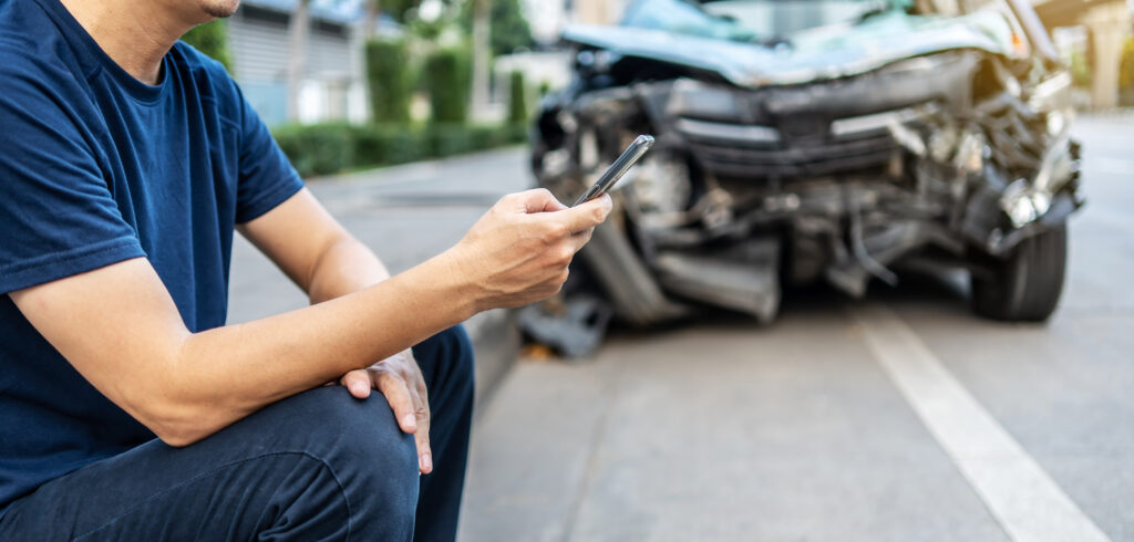 Man Sitting next to a car accident while calling a Denver car accident attorney